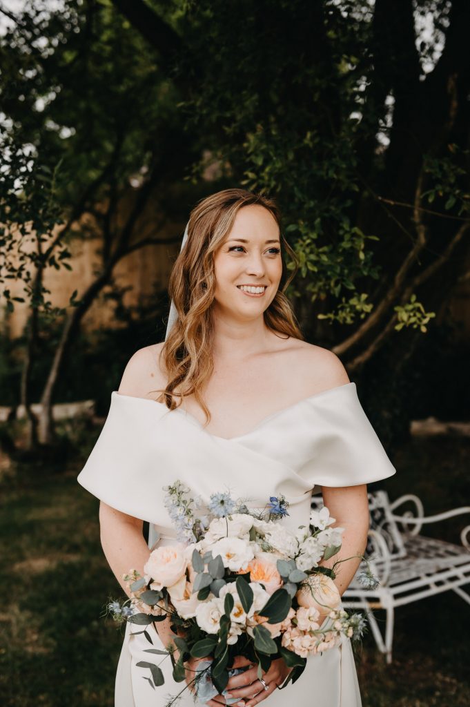 Relaxed and natural wedding portrait. Bride looks to one side with an off the shoulder dress and floral bouquet. 
