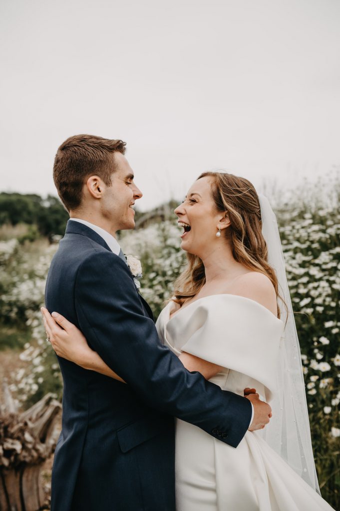 Fun and candid wedding portrait. Couple hug each other closely whilst laughing together. 