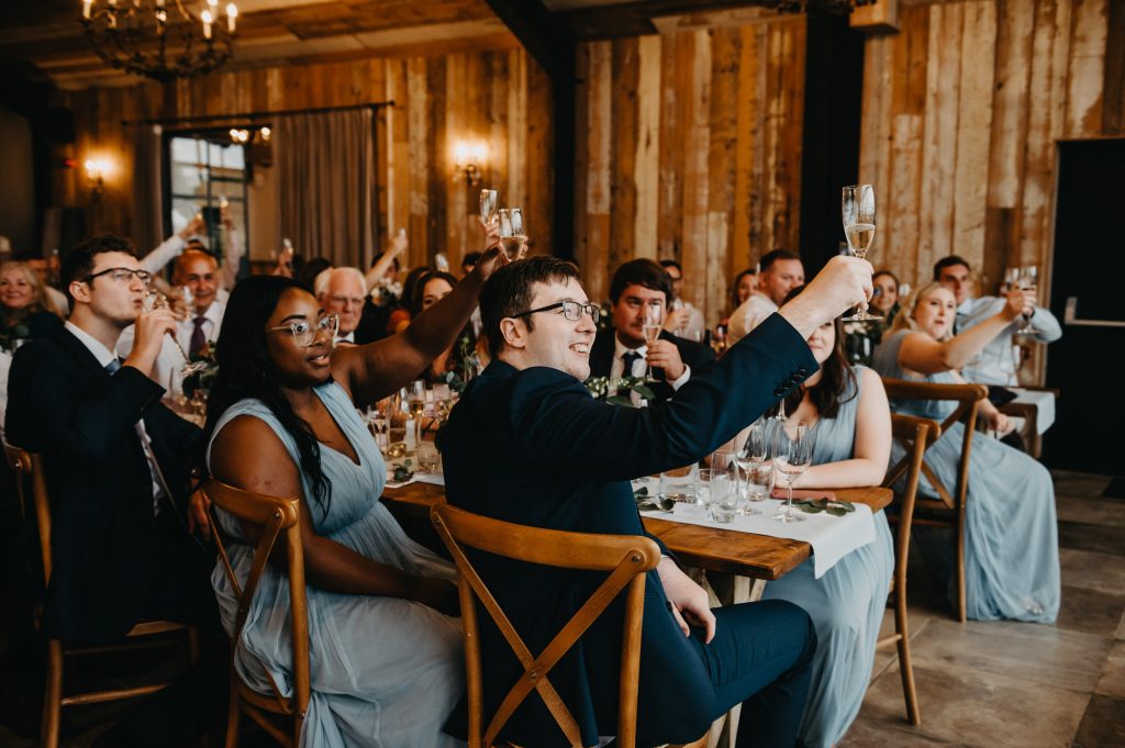 Guests hold up glasses and cheers with the toast at wedding speech.