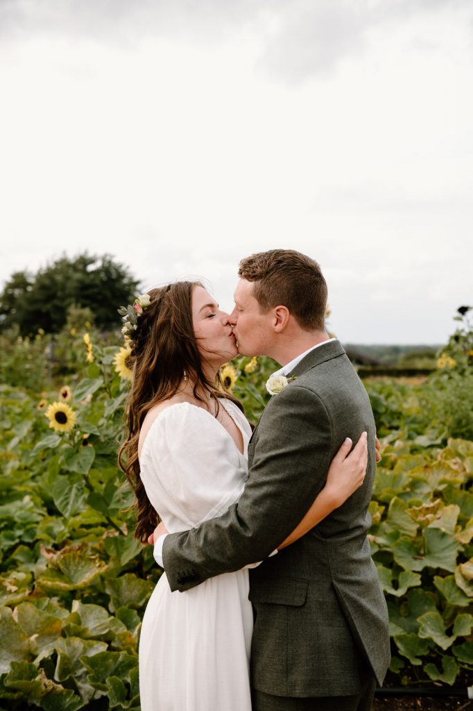 Couple Kiss in Sunflower Field During Couples Portraits - RHS Wisley Garden Wedding