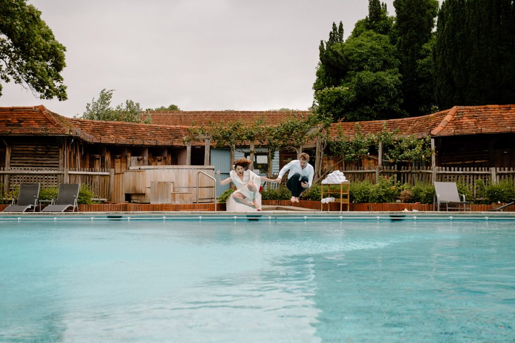 Wedding Couple Jump in The Pool With Wedding Outfits On - Great Fosters Wedding