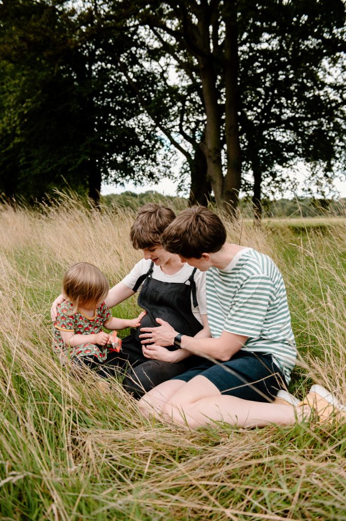 LGBTQ Family Portrait - Child and partner hold mothers pregnant stomach.